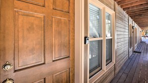 A wooden door with a white frame and a peephole, leading to a covered porch with wooden beams and windows. - Walk to Marina: Rustic Grand Lake Retreat! (Grand Lake)