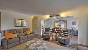 Un salon comprenant un canapé, un pouf et deux fauteuils en cuir. Au fond, on aperçoit un coin repas avec une table et des chaises.