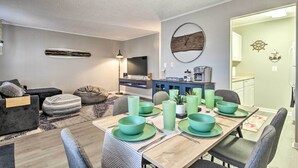 A modern living room with a dining area, featuring a wooden dining table set with teal bowls and plates, a grey sofa, and a flat-screen TV mounted on the wall. - 1/2 Mi to Ocean City Beach! Family-friendly Haven (Ocean City)