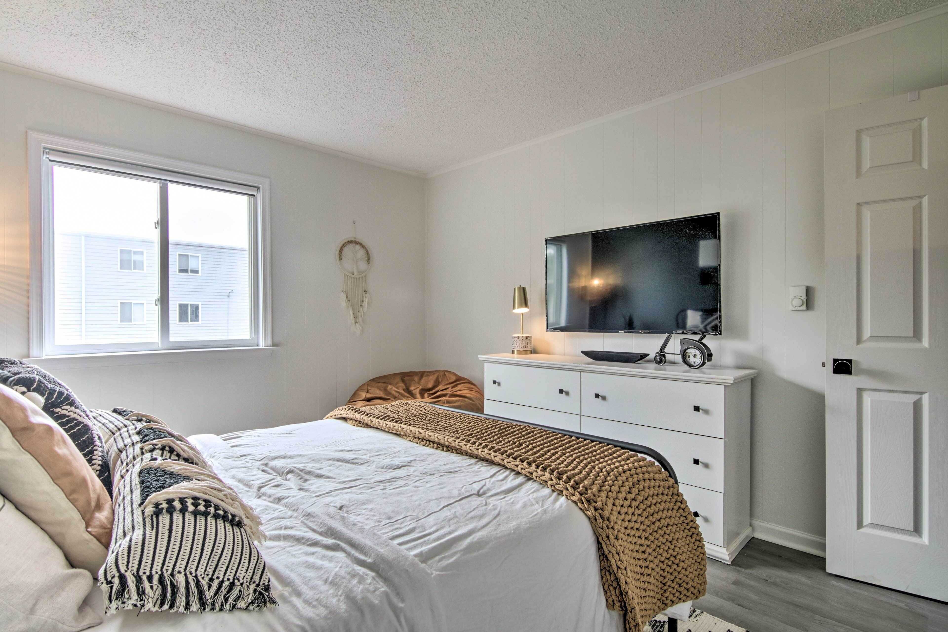 Un dormitorio con cama, cómoda, televisor y ventana.