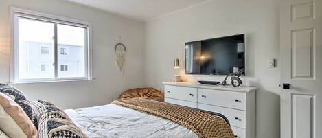 Un dormitorio con cama, cómoda, televisor y ventana.