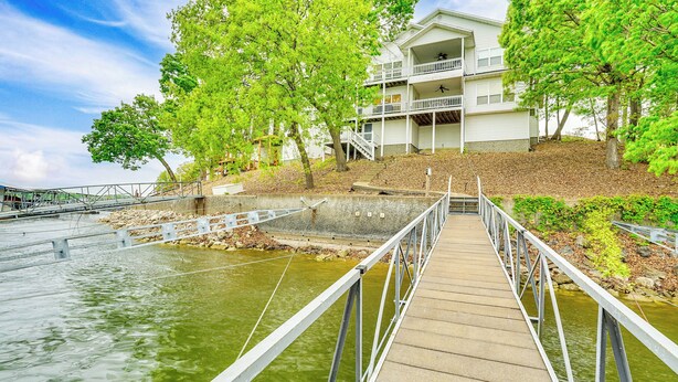 A wooden bridge leading to a white building with balconies, surrounded by trees and a body of water. - Water Sports On-site! Lake of the Ozarks Townhome (Lake Ozark)