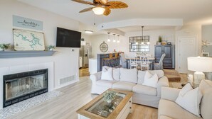 A modern living room with a fireplace, white sofas, a coffee table, and a ceiling fan. - Water Sports On-site! Lake of the Ozarks Townhome (Lake Ozark)