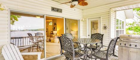 A covered patio with a dining table and chairs, a grill, and a view of the lake.