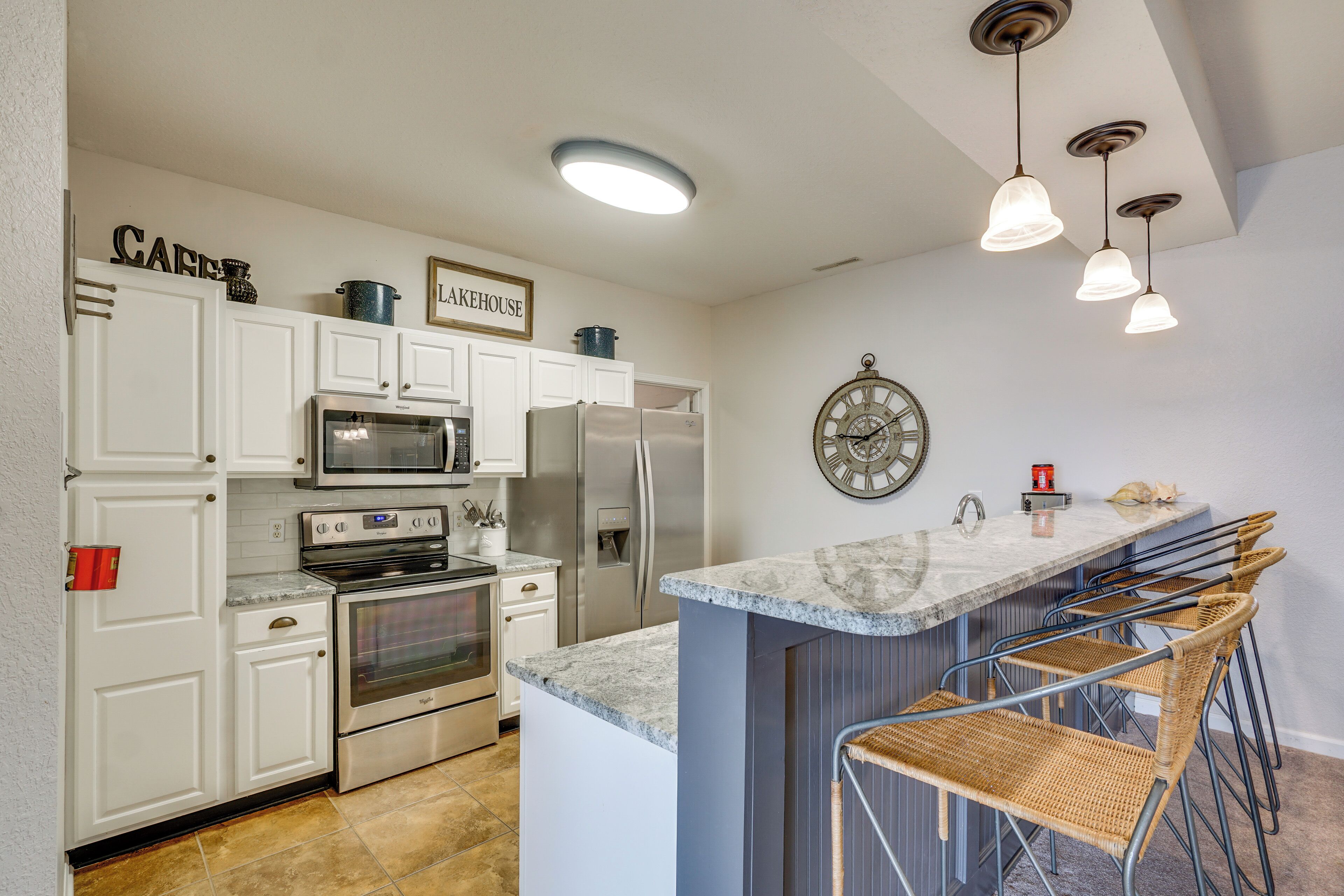 A modern kitchen with white cabinetry, stainless steel appliances, a marble countertop, and a bar area with wicker chairs.