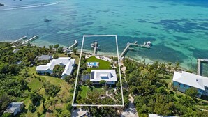 Une vue aérienne d’une propriété située sur la côte, offrant une vue dégagée sur l’océan, un quai et plusieurs bâtiments.
