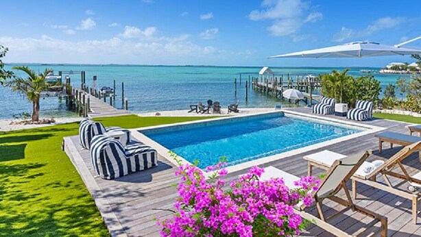 Un espace piscine avec vue sur l’océan, des chaises longues et une terrasse en bois.