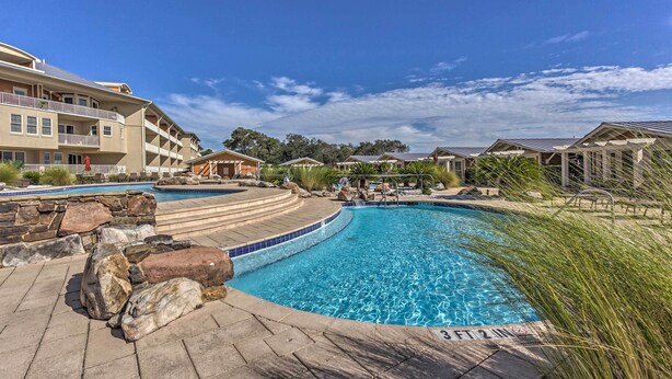A swimming pool with a stone border, a clear blue sky, and a building with balconies in the background. - 30A Retreat w/ Patio & Resort Amenities! (Santa Rosa Beach)