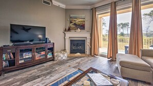 A living room with a fireplace, a television, and a balcony with curtains. - 30A Retreat w/ Patio & Resort Amenities! (Santa Rosa Beach)