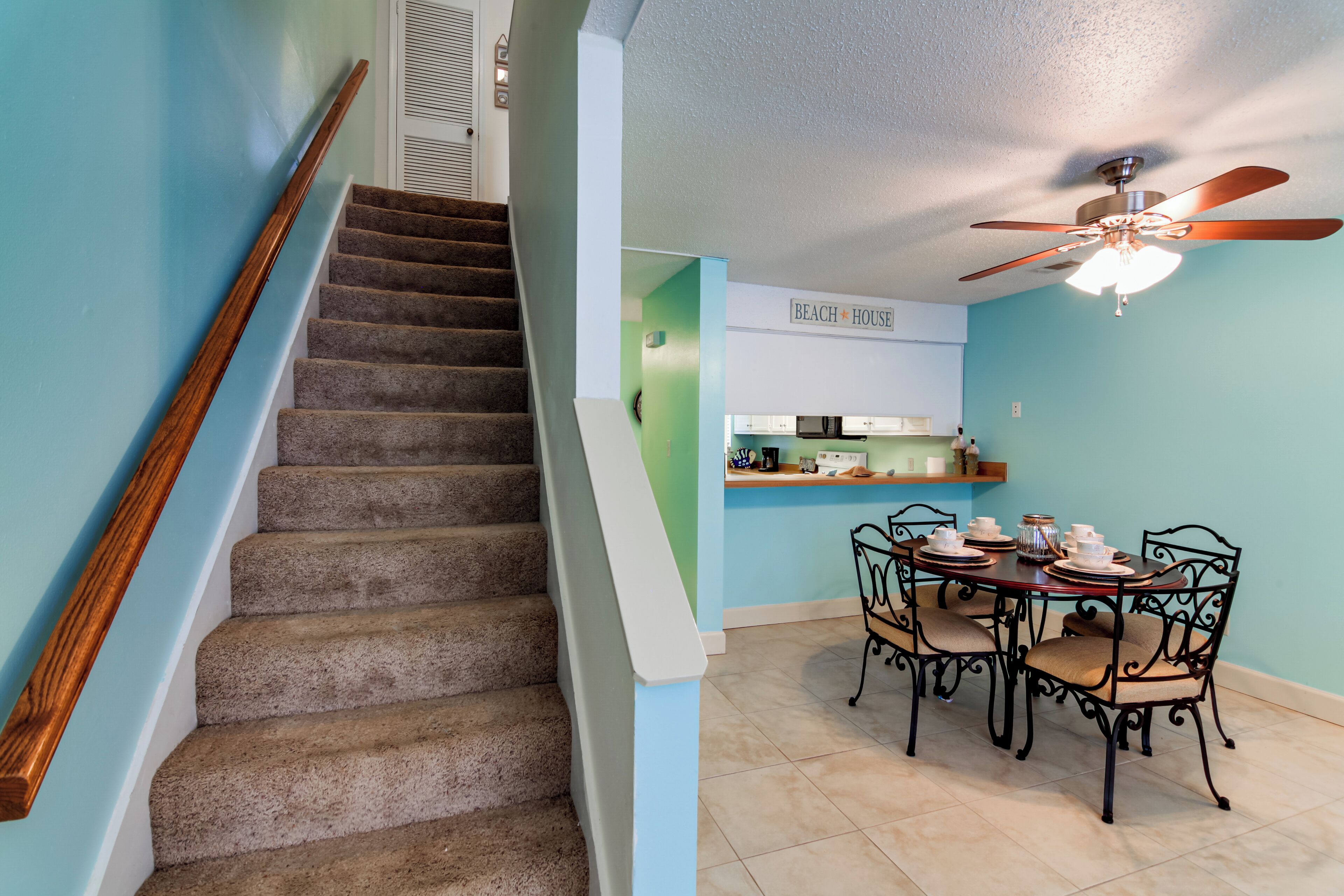 A staircase with a wooden handrail leading to a dining area with a table set for four.