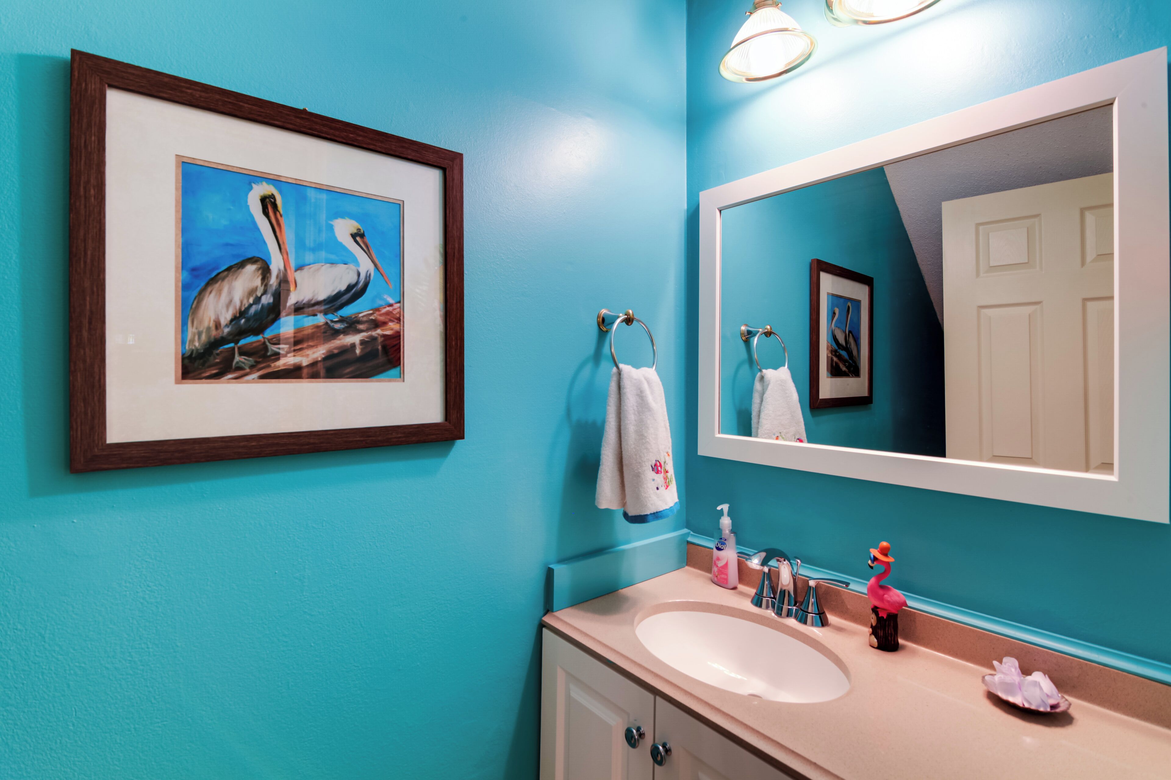 A bathroom with a turquoise wall, a framed painting of pelicans, a sink, and a mirror.