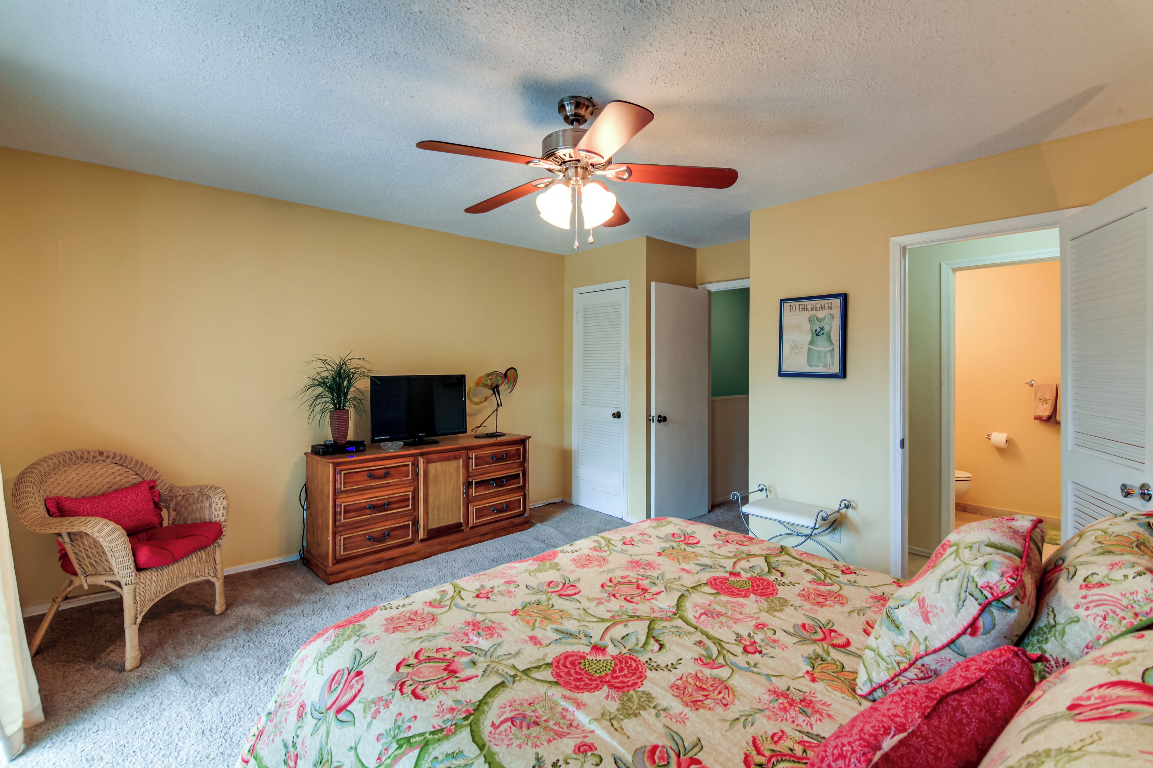 A bedroom with a bed, a chair, a dresser, a ceiling fan, and a door.