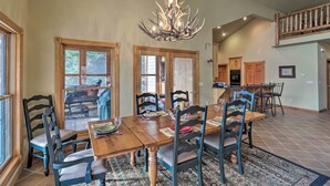A spacious dining area with a large wooden table, multiple chairs, and a unique antler chandelier. - Kalispell Riverfront Home by Glacier National Park (Kalispell)