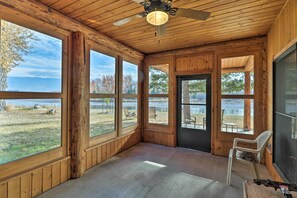 Une cabane en bois dotée de grandes fenêtres, d’un ventilateur de plafond et offrant une vue sur un lac.