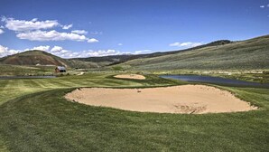 A golf course with bunkers, a pond, and a building in the background. - Ski-in/out Granby Ranch Condo w/ Balcony! (Granby)