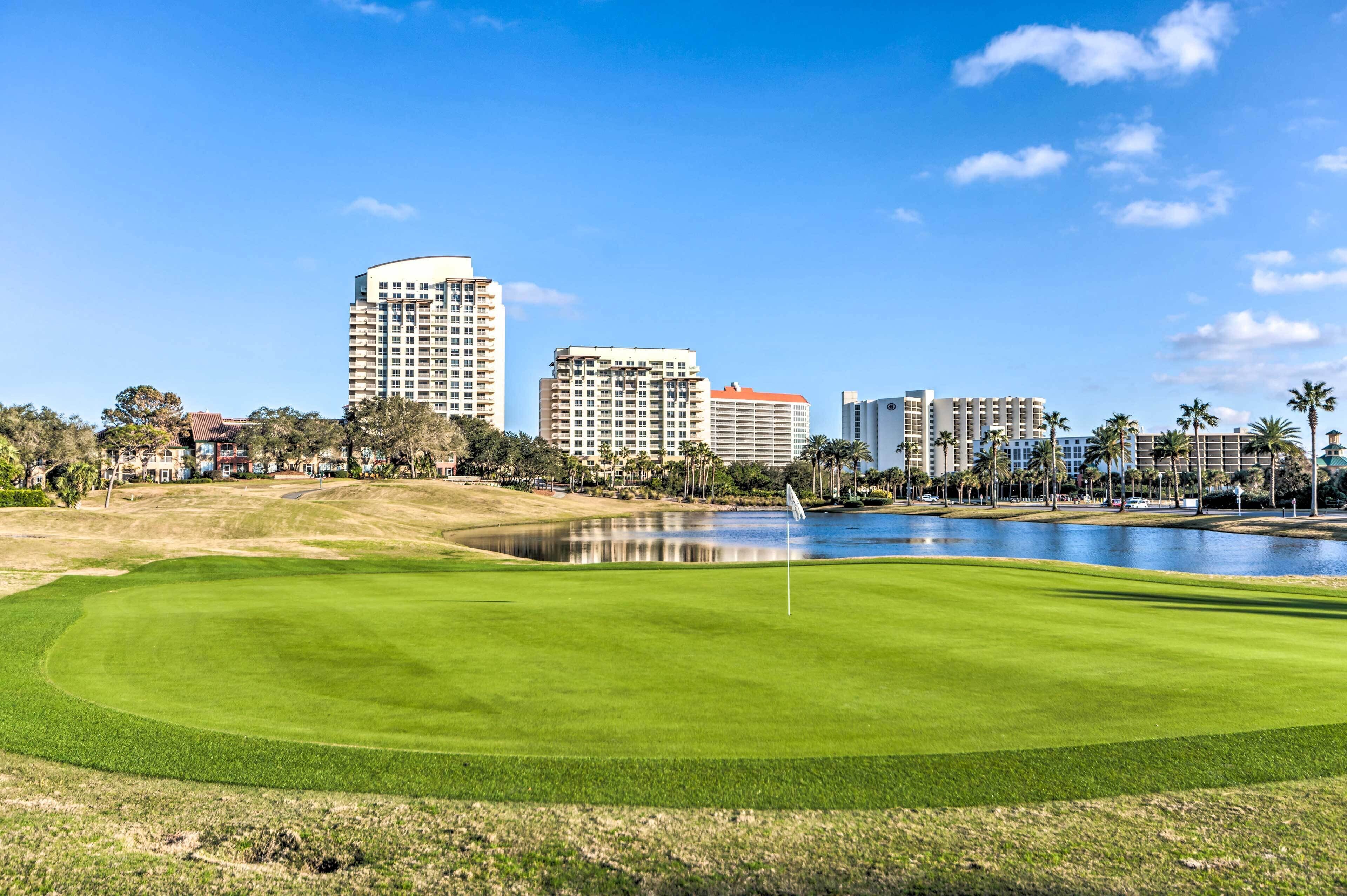 A golf course with a water hazard, surrounded by high-rise buildings and palm trees.