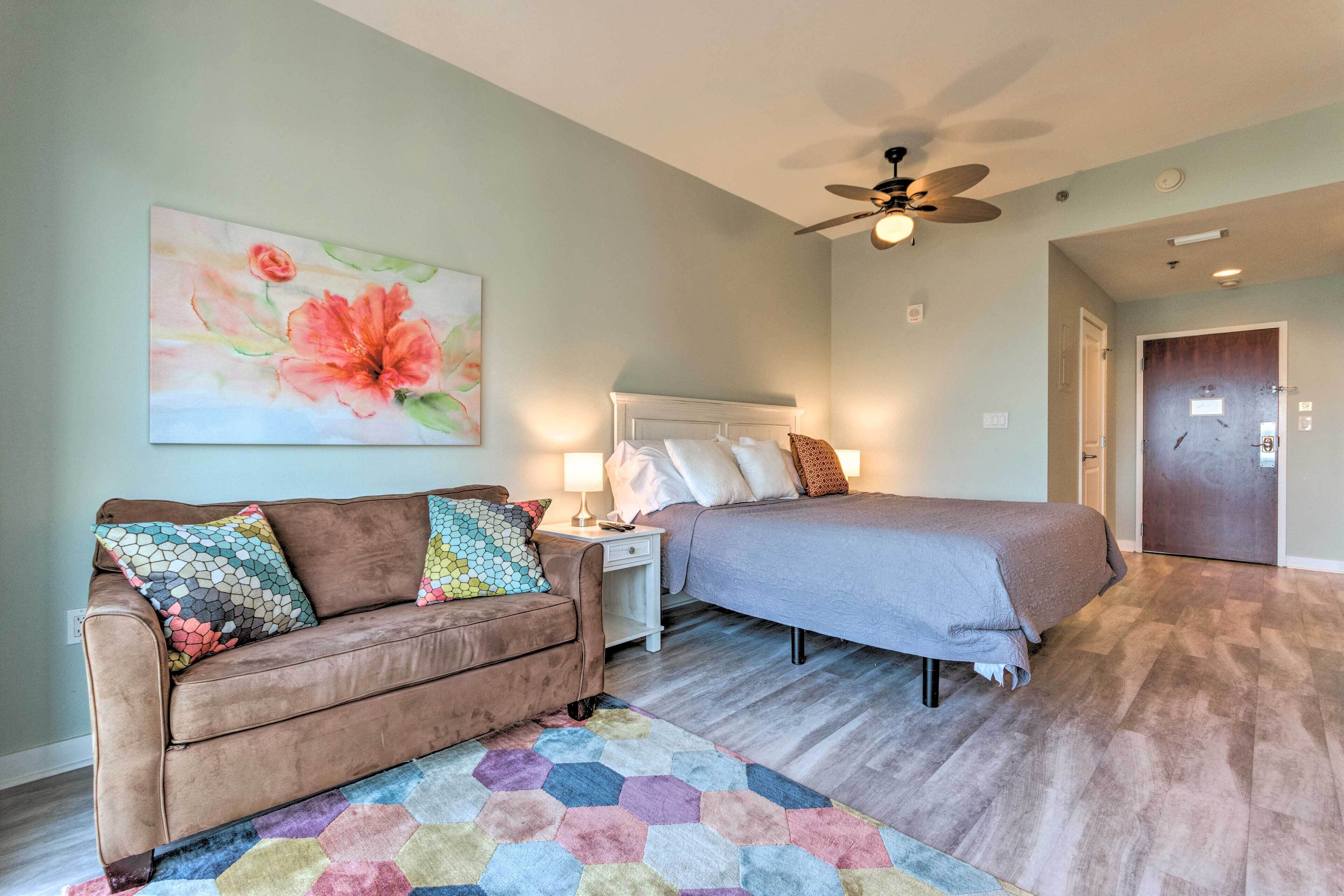 A bedroom with a bed, a sofa, a nightstand, a ceiling fan, and a door.