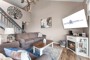 Ein Wohnzimmer mit Sofa, Couchtisch, Kamin und einem an der Wand befestigten Fernseher.