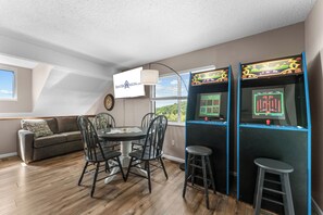 Ein Zimmer mit Esstisch, Stühlen, einer Couch, Spielautomaten und einem Fernsehbildschirm, der eine Website zeigt.
