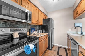 A modern kitchen with stainless steel appliances, wooden cabinets, and a black refrigerator.