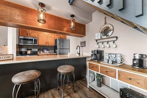Une cuisine dotée de meubles en bois, d’un réfrigérateur en acier inoxydable, d’un four à micro-ondes et d’un espace dédié à la préparation du café.