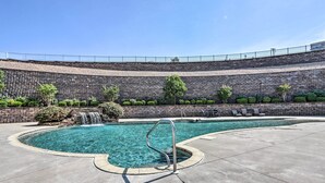 A swimming pool with a metal handrail, surrounded by a stone wall and a clear blue sky.