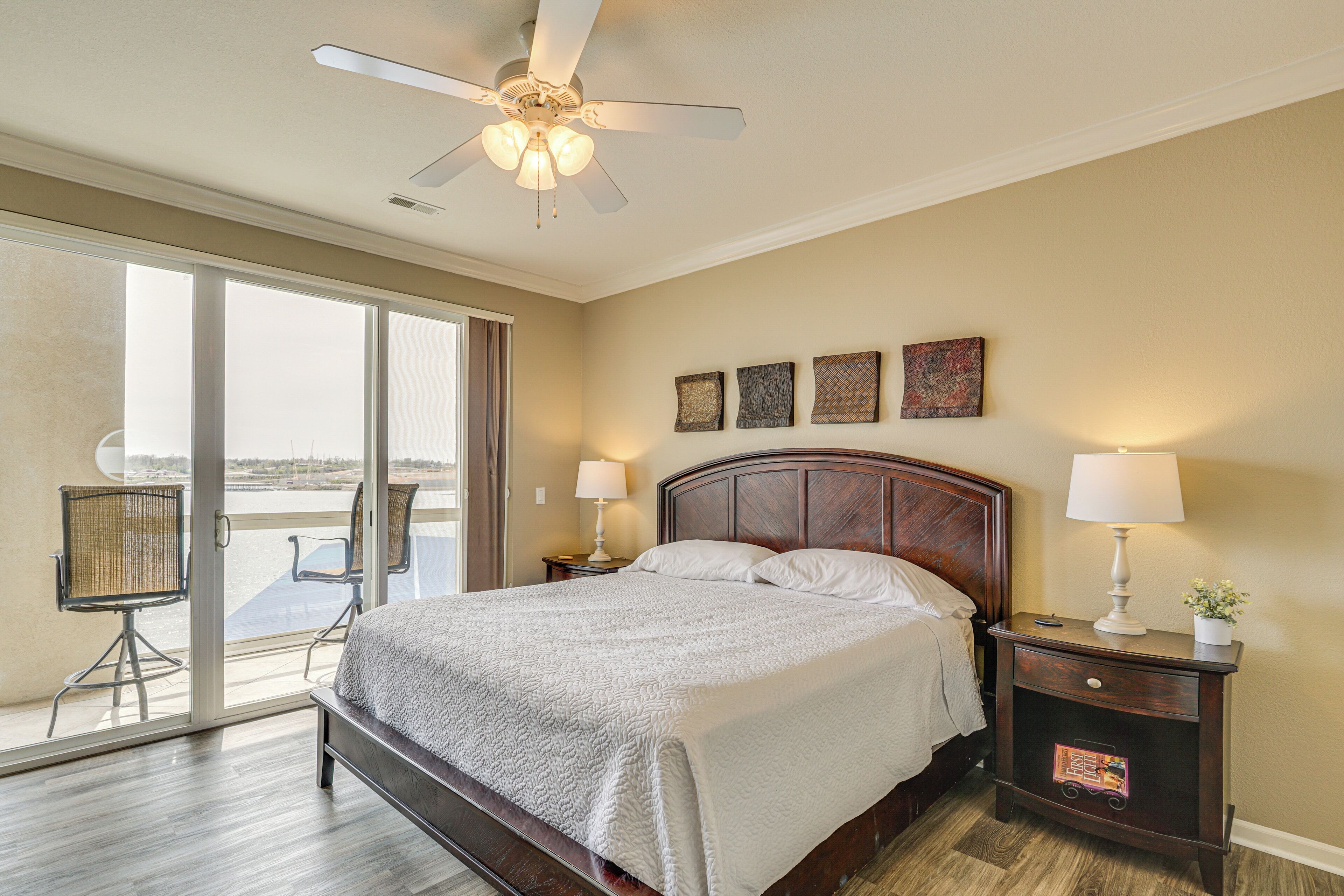 A bedroom with a bed, two bedside tables with lamps, a ceiling fan, and a view through a sliding glass door.
