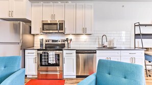 A modern kitchen with white cabinets, stainless steel appliances, and blue chairs.