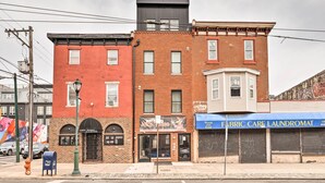A row of buildings with a red brick facade, a black metal structure on top, and a blue storefront with a sign reading "FABRIC CARE LAUNDRYMAT."