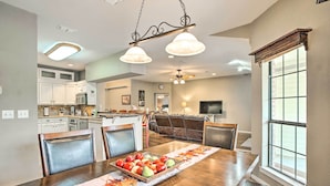 A dining area with a wooden table, chairs, and a fruit basket. There is a kitchen in the background with white cabinets and a window. - Gainesville Home w/ Outdoor Oasis, 16 Mi to Lake (Gainesville)
