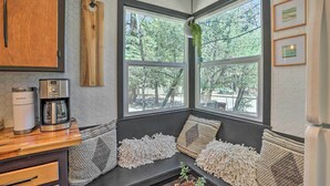 Uma cozinha acolhedora com um banco embutido, uma cafeteira Keurig e vista para árvores por grandes janelas.