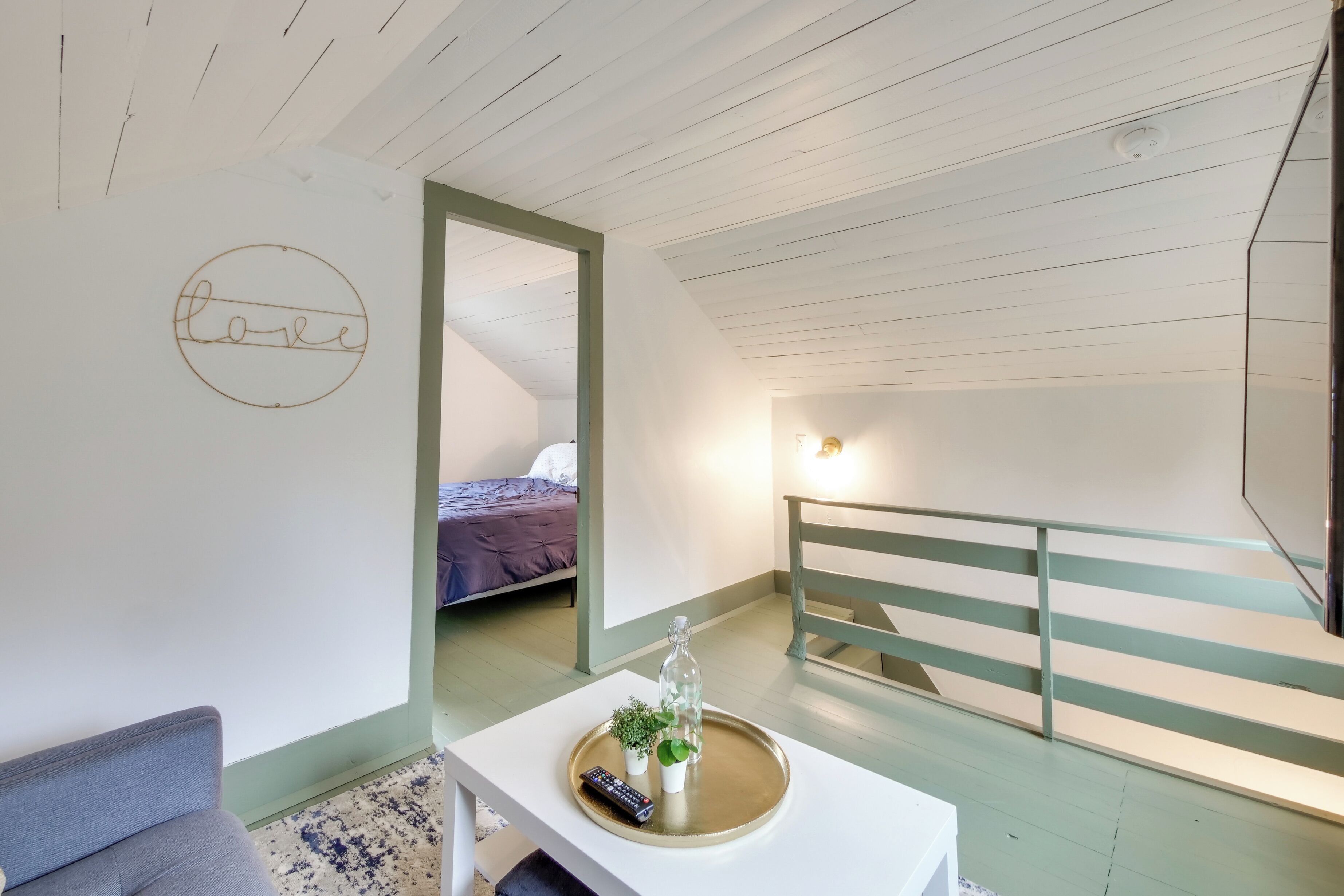 A room with a bed, a small table with a tray, a remote control, and a wall with a 'love' sign.