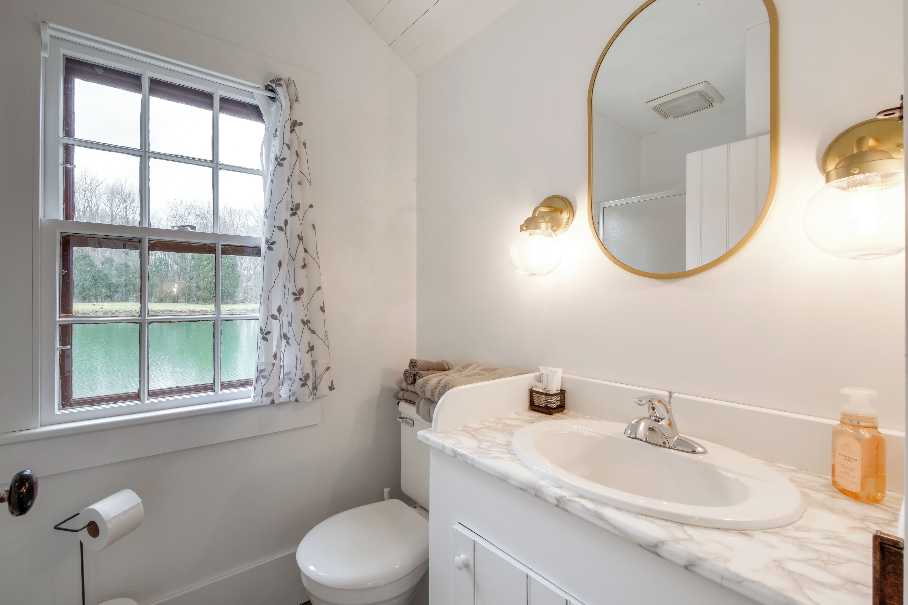 Un baño con ventana, inodoro, lavamanos y espejo.