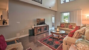 A spacious living room with a high ceiling, a large flat-screen TV, a wooden entertainment center, a round coffee table, and a large window with curtains. - Legends Golf & Resort Townhouse: Resort Amenities! (Myrtle Beach)
