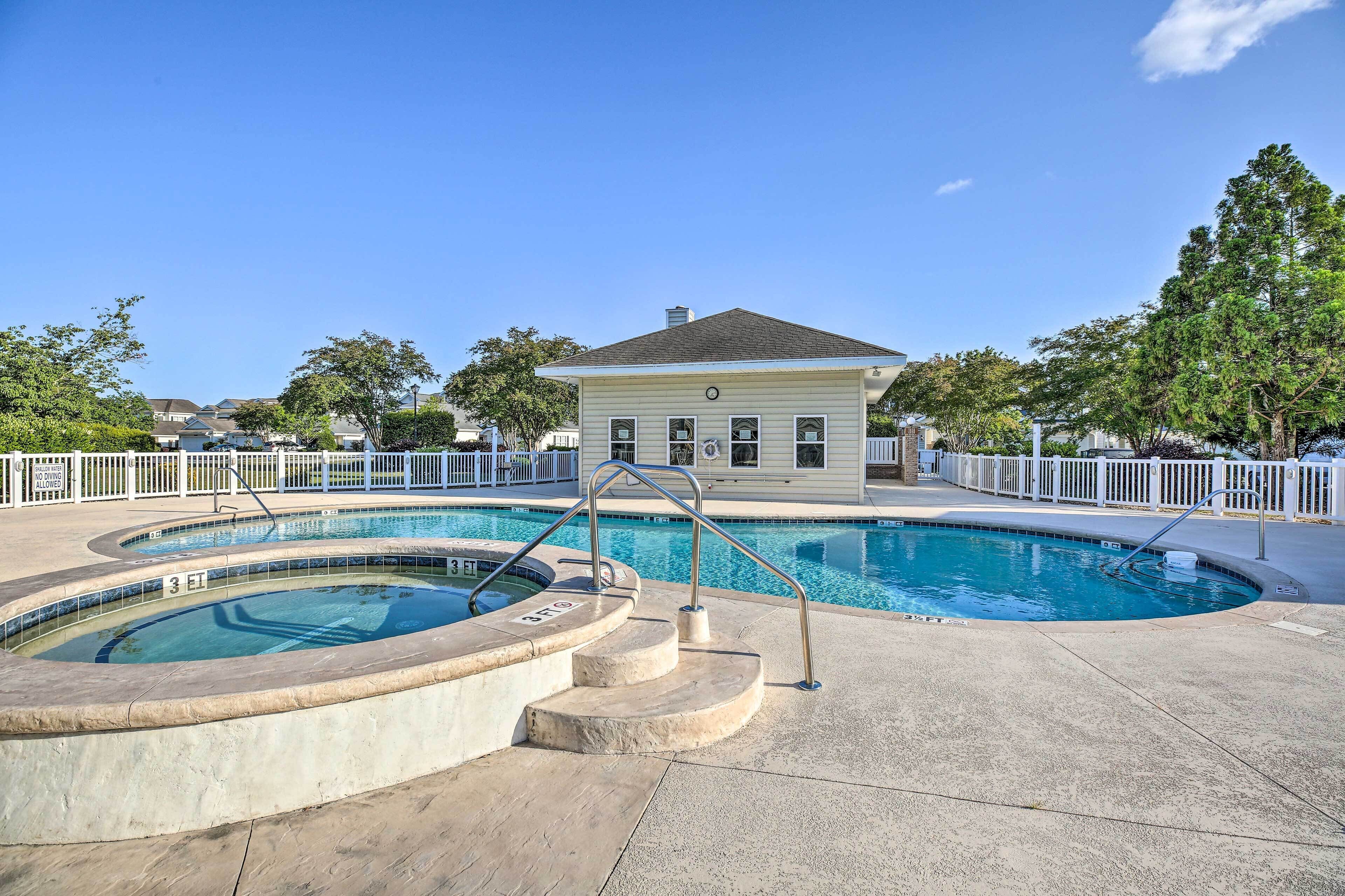 A swimming pool with a hot tub, surrounded by a white fence and trees.