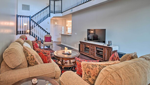 A spacious living room with a high ceiling, a staircase, and a flat-screen TV. - Legends Golf & Resort Townhouse: Resort Amenities! (Myrtle Beach)
