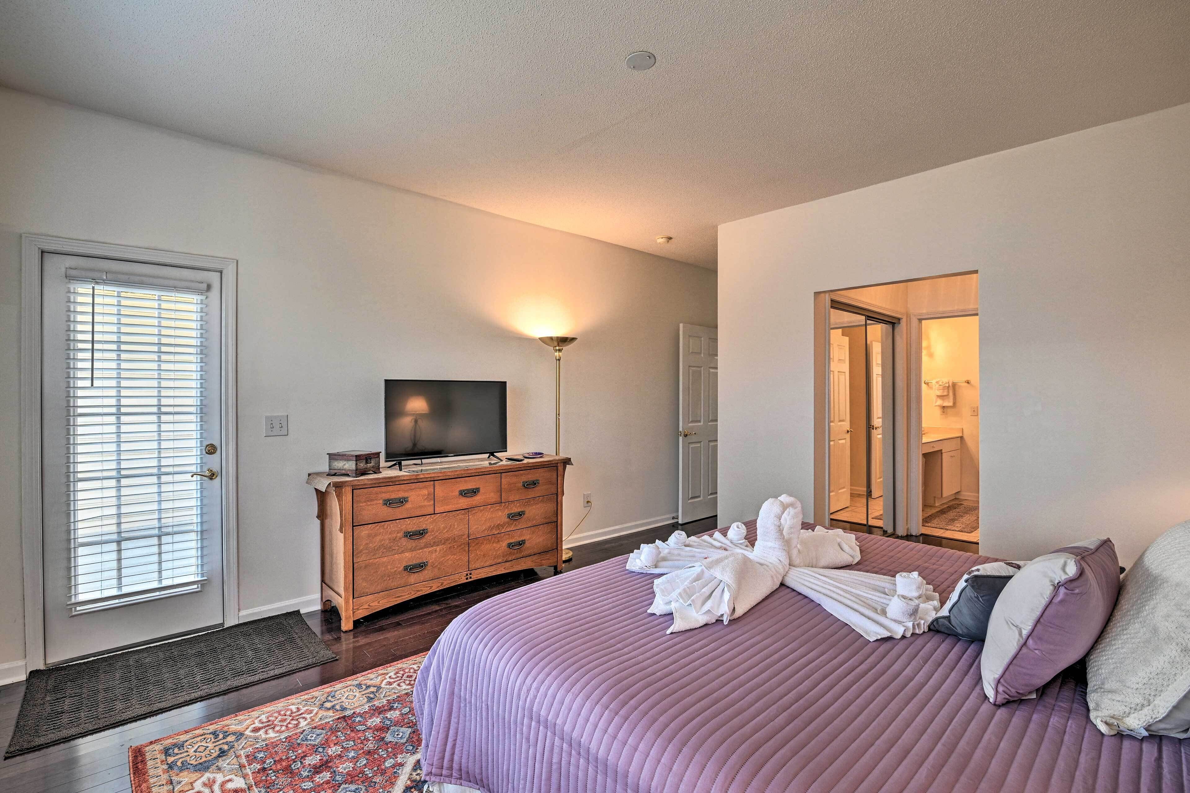 A bedroom with a bed, a dresser, a television, and a door leading to a bathroom.