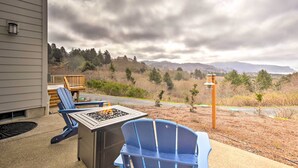 Un patio al aire libre con dos sillas Adirondack, una chimenea y vistas a una ladera boscosa.