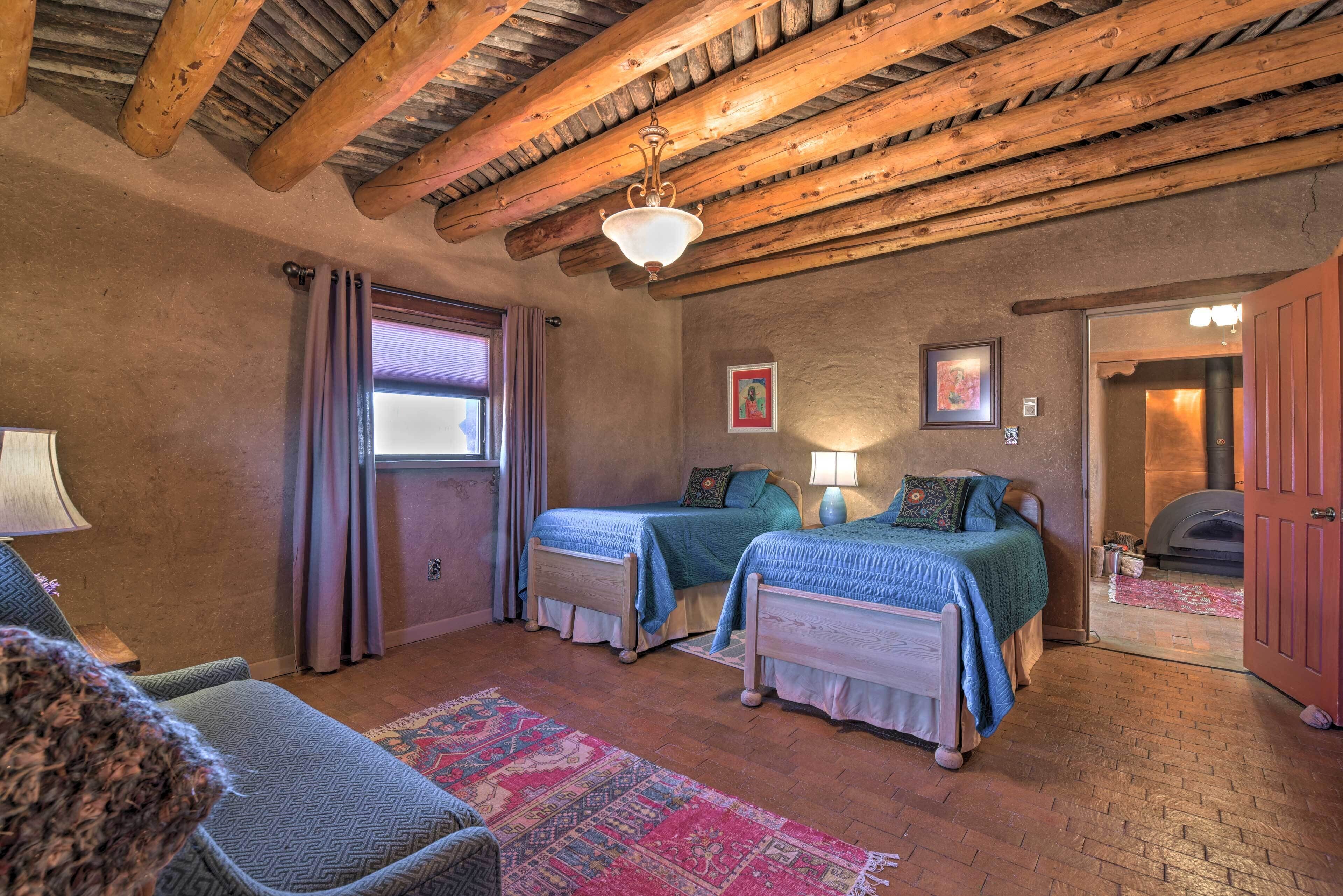 A cozy room with two beds, wooden beams on the ceiling, a fireplace, and a window with curtains.