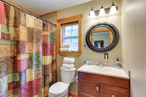A bathroom with a quilted shower curtain, a toilet, a sink with toiletries, and a mirror. - Rustic Cabin w/ Hot Tub - 7 Miles to Hocking Hills (Logan)