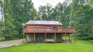 A log cabin with a porch, stone foundation, and a satellite dish.