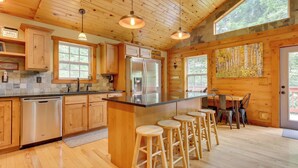 A kitchen with wooden cabinets, a stainless steel refrigerator, and a bar area with stools.
