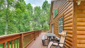 A wooden deck with a picnic table and chairs, surrounded by a wooden railing, overlooking a forested area.