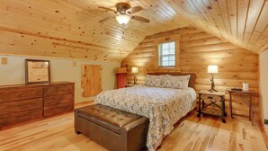 A log cabin bedroom with a bed, nightstands, a dresser, and a ceiling fan.