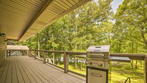 Eine überdachte Holzterrasse mit einem Grill und Blick auf einen von Bäumen umgebenen See.