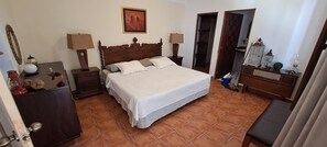 A bedroom with a large bed, wooden headboard, two bedside tables with lamps, a dresser, and a mirror. - The Orchid Hotel (Antigua Guatemala)