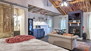 A cozy bedroom with a large bed, a sofa, a fireplace, and a kitchen area in the background. - Fredericksburg 'regan Cottage' w/ Hot Tub! (Fredericksburg)