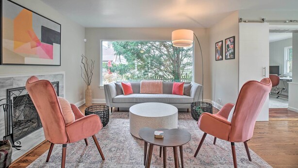 A modern living room with a grey sofa, two pink armchairs, a round coffee table, and a fireplace.