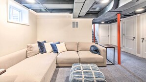 A modern living room with a beige sectional sofa, a small table, and a patterned ottoman.