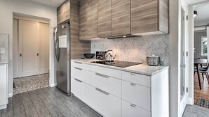 A modern kitchen with white cabinetry, a stainless steel refrigerator, a built-in stove, and a marble backsplash.